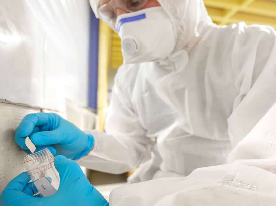 Asbestos surveyor taking a sample of building material in small plastic bag, standard survey to locate any presence and the extent of materials containing asbestos (ACMs)