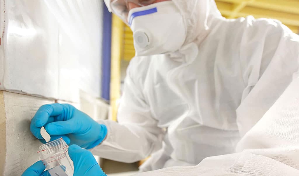 Asbestos surveyor taking a sample of building material in small plastic bag, standard survey to locate any presence and the extent of materials containing asbestos (ACMs)